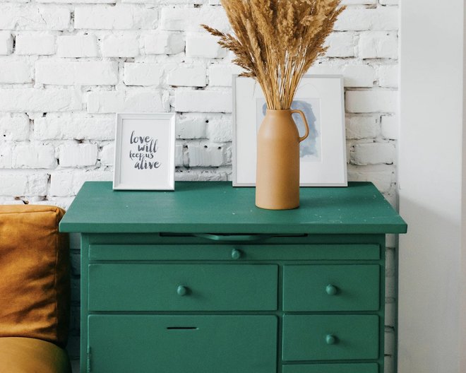 image of a set of green drawers with picture frames and a vase of pampas grass